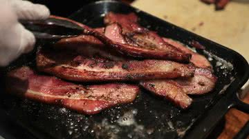 Imagem ilustrativa de pessoa cozinhando bacon - Getty Images